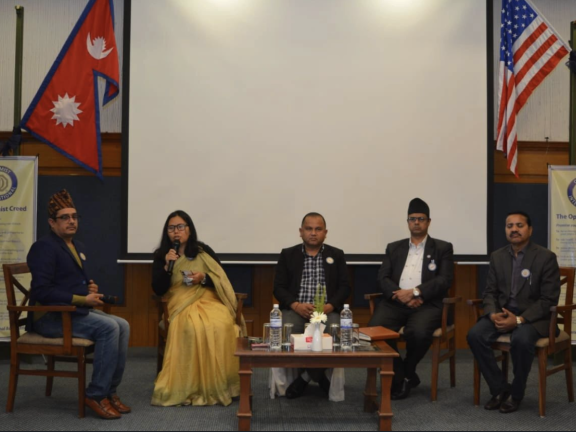 Five people are on a panel. A woman speaks into a microphone. Photo: Jhabindra Bhusal.