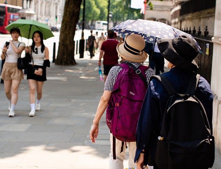People walk along a street holding umbrellas to protect themselves from the sun